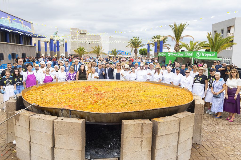 La paella en primer plano junto al grupo de gobierno y cocineros tras acabar la cocción