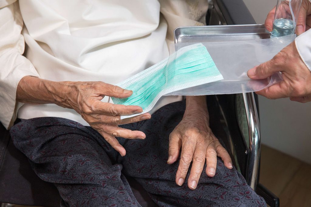 Elderly woman get a mask from caregiver to protect from coronavi